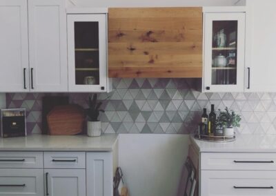 Custom kitchen with some clear-faced cupboard doors and a decorative, wooden hood fan.