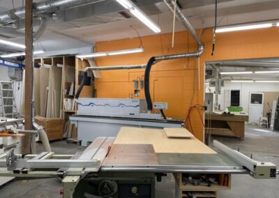 Photo of wood word machines and wood against an orange wall in the Steinegg Cabinets shop in Nelson BC