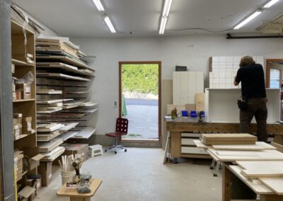 Photo of the interior of the Steinegg Cabinets shop in Nelson BC. Shelves full of wood are visible.