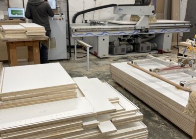 Photo of the CNC machine in the Steinegg Cabinets shop, Nelson BC. Stacks of wood for custom cabinets are visible too.